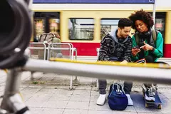 male and female looking at phone while sitting on a bench on a train platform.
